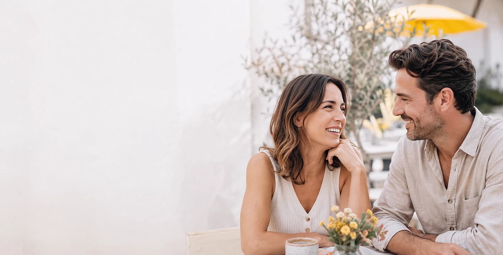 Two people laughing together on a sunny café terrace